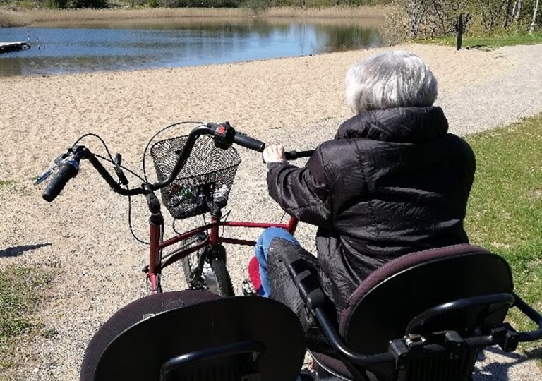 En ældre dame på cykel ved en sø