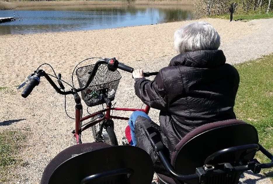 En ældre dame på cykel ved en sø